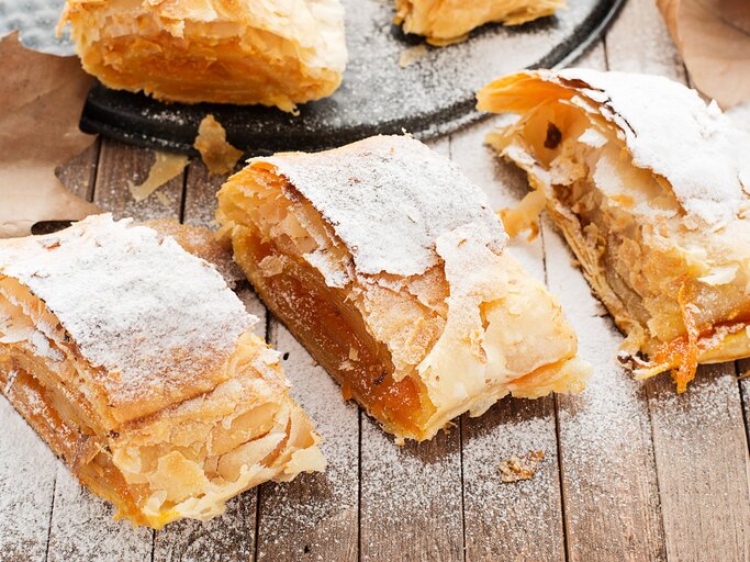 Leckerer Kürbis-Strudel auf einem Holztisch mit Herbstblättern von schräg oben fotografiert. | © Shutterstock/ nelea33