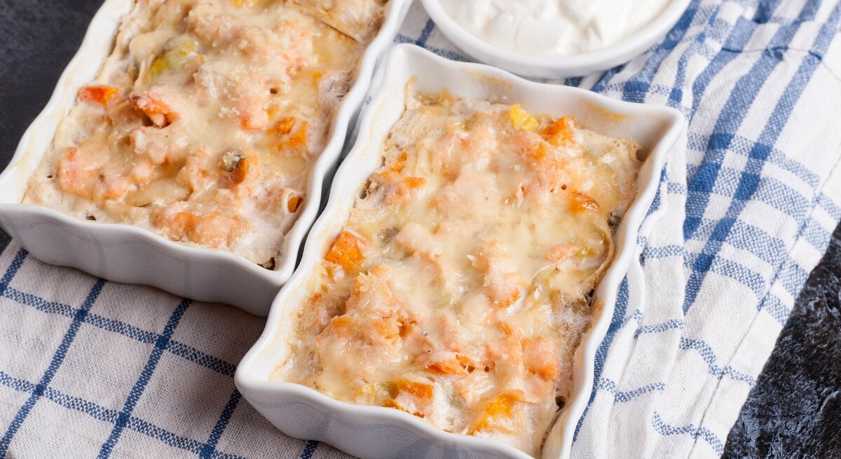 Zwei Auflaufformen mit Kürbis-Lachs-Auflauf auf einem blau-weiß-gestreiften Küchentuch.