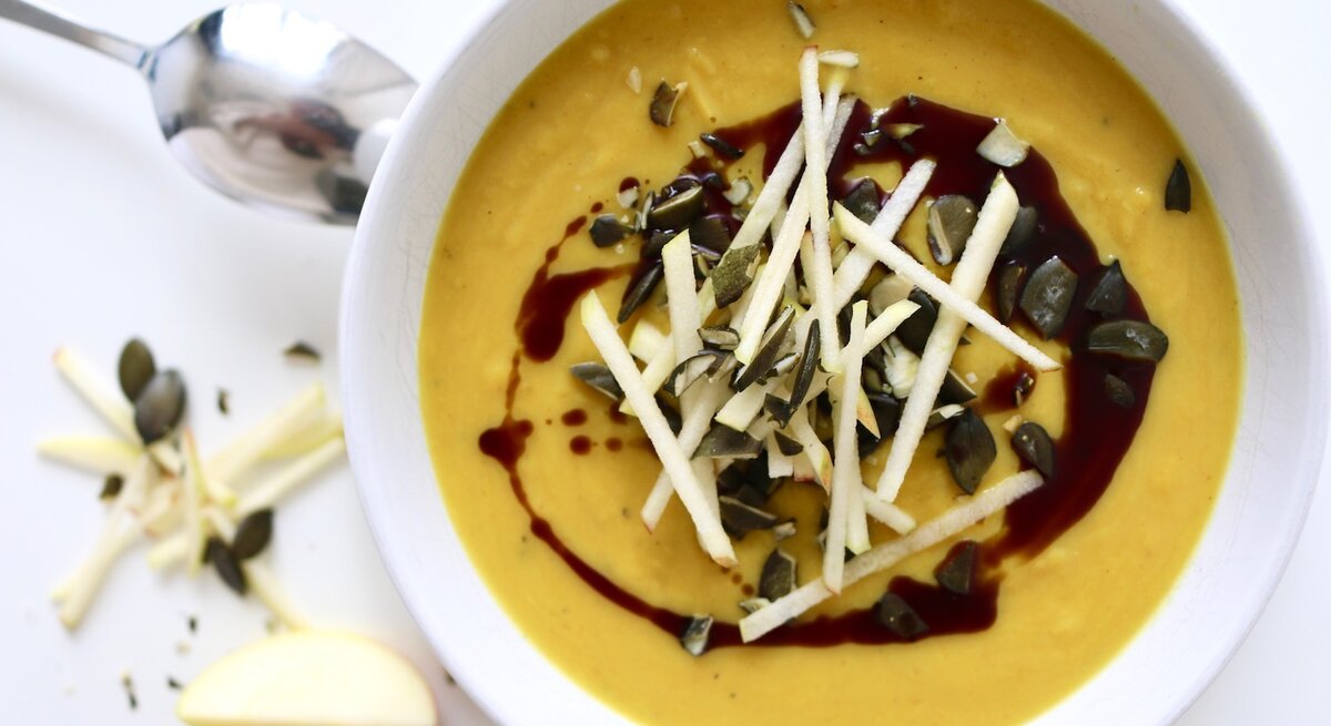 Kürbis-Apfel-Suppe mit Curry in einer Schüssel, dekoriert mit Samen und Kernen, von oben fotografiert.