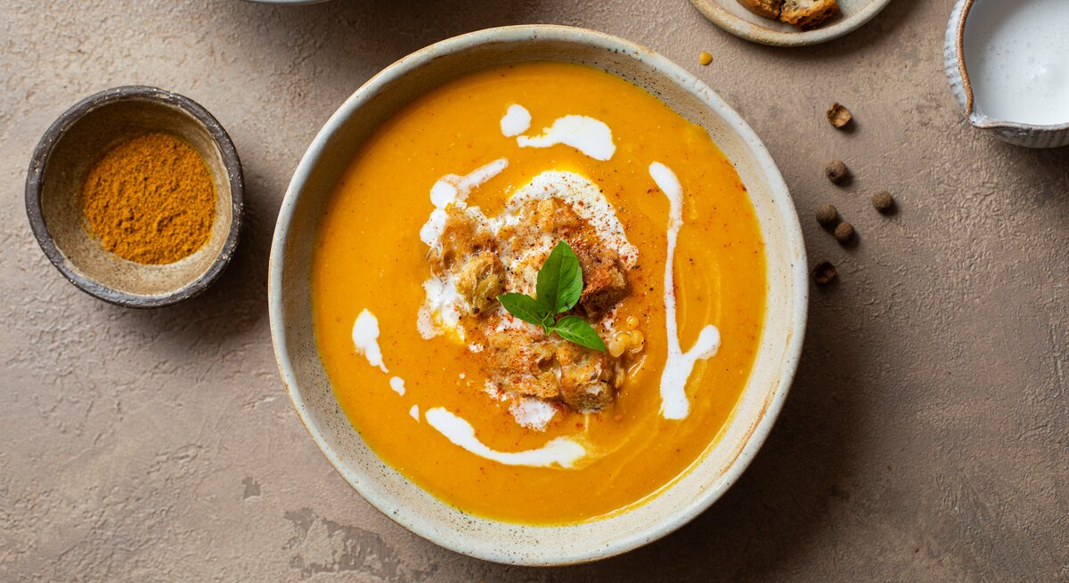 Kürbis-Linsen-Suppe in Schale auf hellbraunem Untergrund.