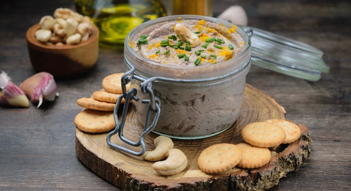 Ein Weckglas mit Cashew-Dressing und Schnittlauch, drumherum Cracker, Cashews, Knoblauch und eine Ölflasche.