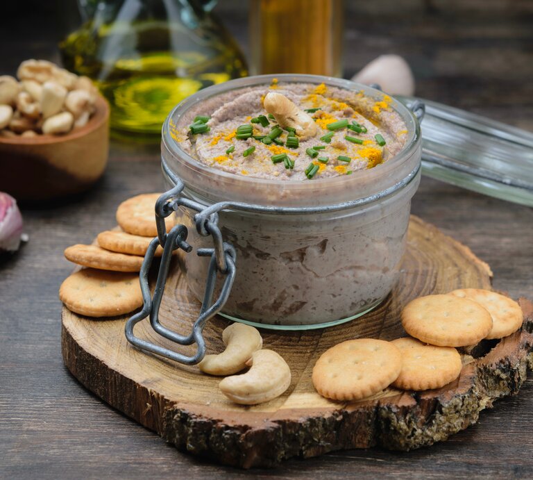 Ein Weckglas mit Cashew-Dressing und Schnittlauch, drumherum Cracker, Cashews, Knoblauch und eine Ölflasche. | © Adobe Stock/ Mila Bond