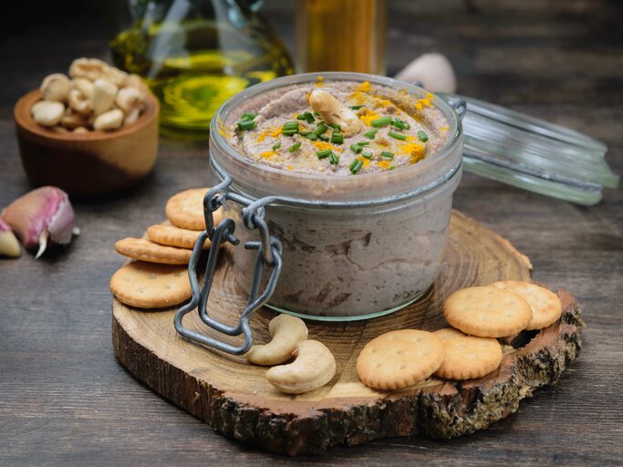 Ein Weckglas mit Cashew-Dressing und Schnittlauch, drumherum Cracker, Cashews, Knoblauch und eine Ölflasche. | © Adobe Stock/ Mila Bond