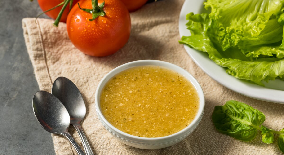 italienisches Knoblauchdressing in kleiner Schale. Daneben Tomaten und Blattsalat. 