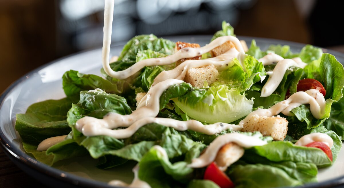Dressing wird auf grünen Salat geträufelt. 
