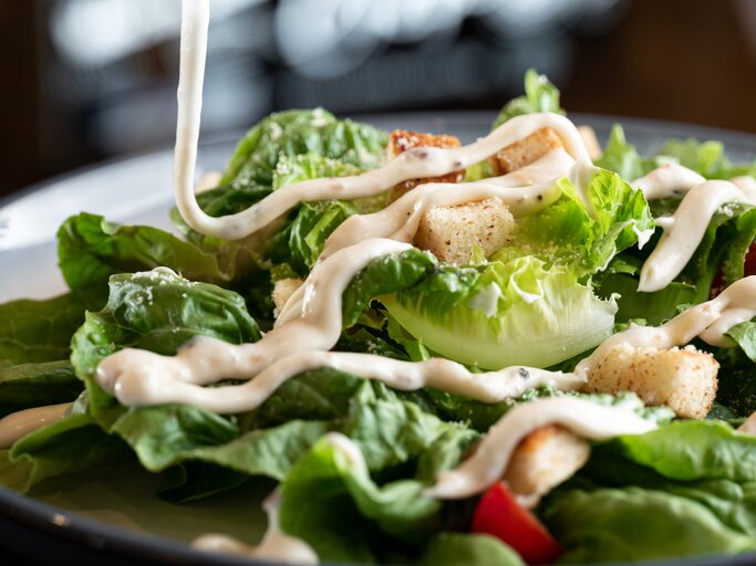 Dressing wird auf grünen Salat geträufelt.  | © Getty Image/Justin Ong