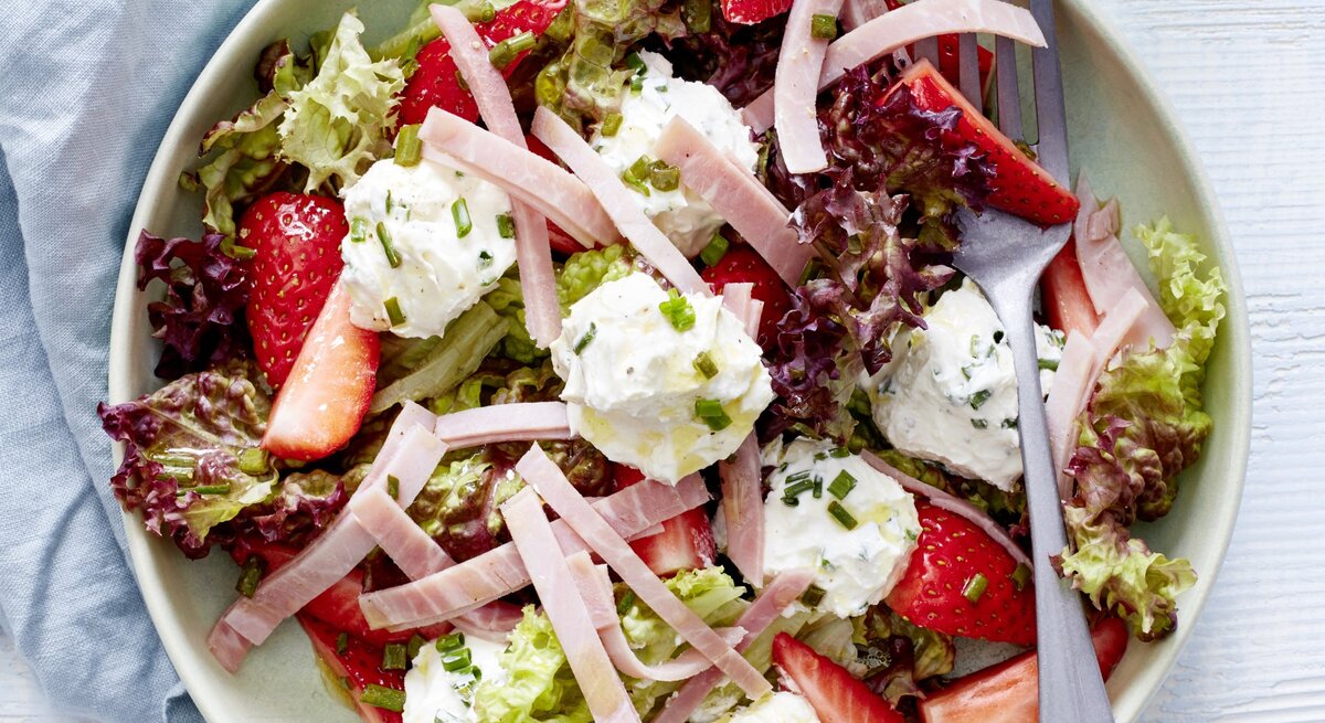 Sommersalat mit Erdbeeren, Frischkäse und Schinken in einer weißen Schale. Darin liegt eine Gabel. 