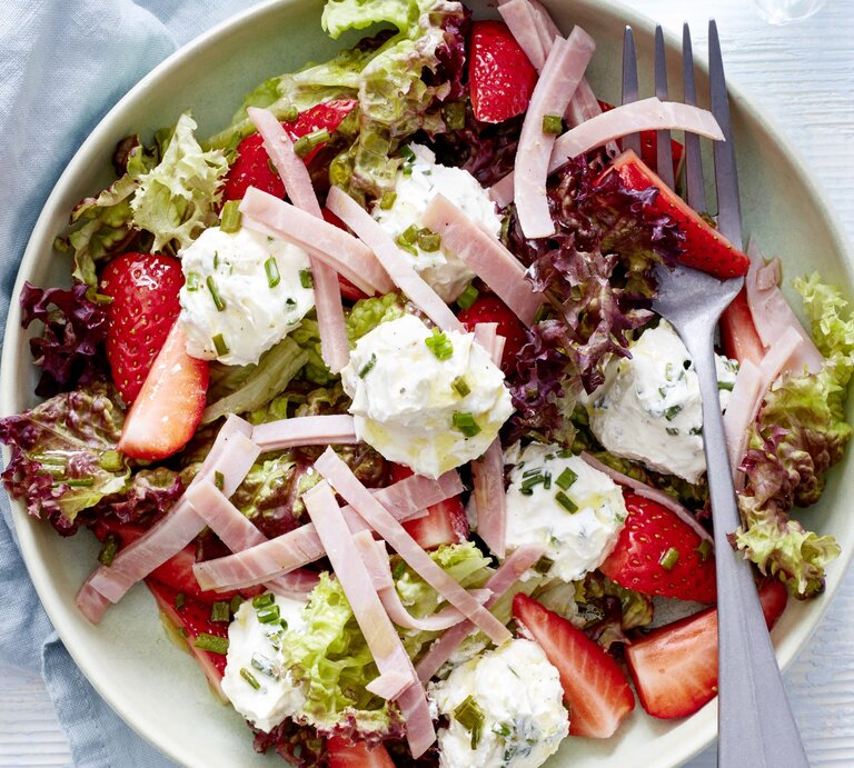 Sommersalat mit Erdbeeren, Frischkäse und Schinken in einer weißen Schale. Darin liegt eine Gabel.  | © EAT CLUB / Isabell Triemer