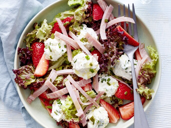 Sommersalat mit Erdbeeren, Frischkäse und Schinken in einer weißen Schale. Darin liegt eine Gabel.  | © EAT CLUB / Isabell Triemer