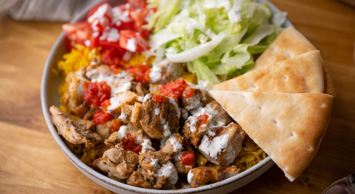 Ein veganer Gyros-Salat mit Sojaschnetzeln, Salat, Reis und Joghurtsoße, dazu Fladenbrot.