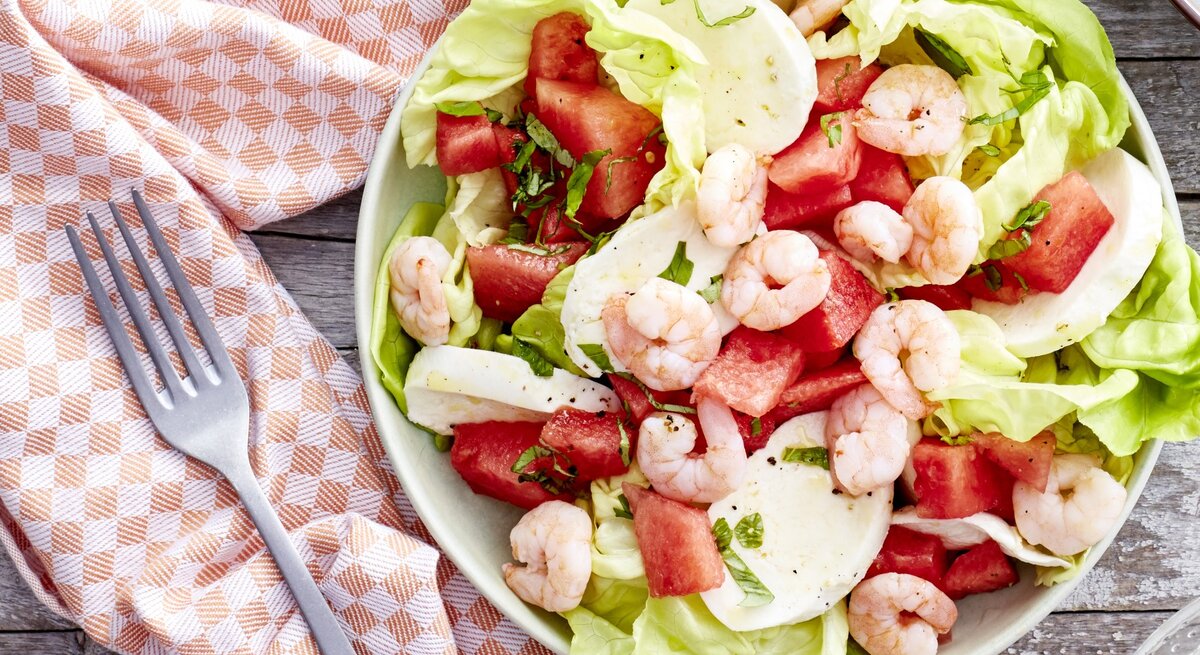 In einer Schüssel ist ein Wassermelonen-Salat mit Mozzarella angerichtet. Er ist mit Garnelen garniert.