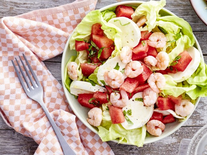 In einer Schüssel ist ein Wassermelonen-Salat mit Mozzarella angerichtet. Er ist mit Garnelen garniert. | © EAT CLUB / Isabell Triemer