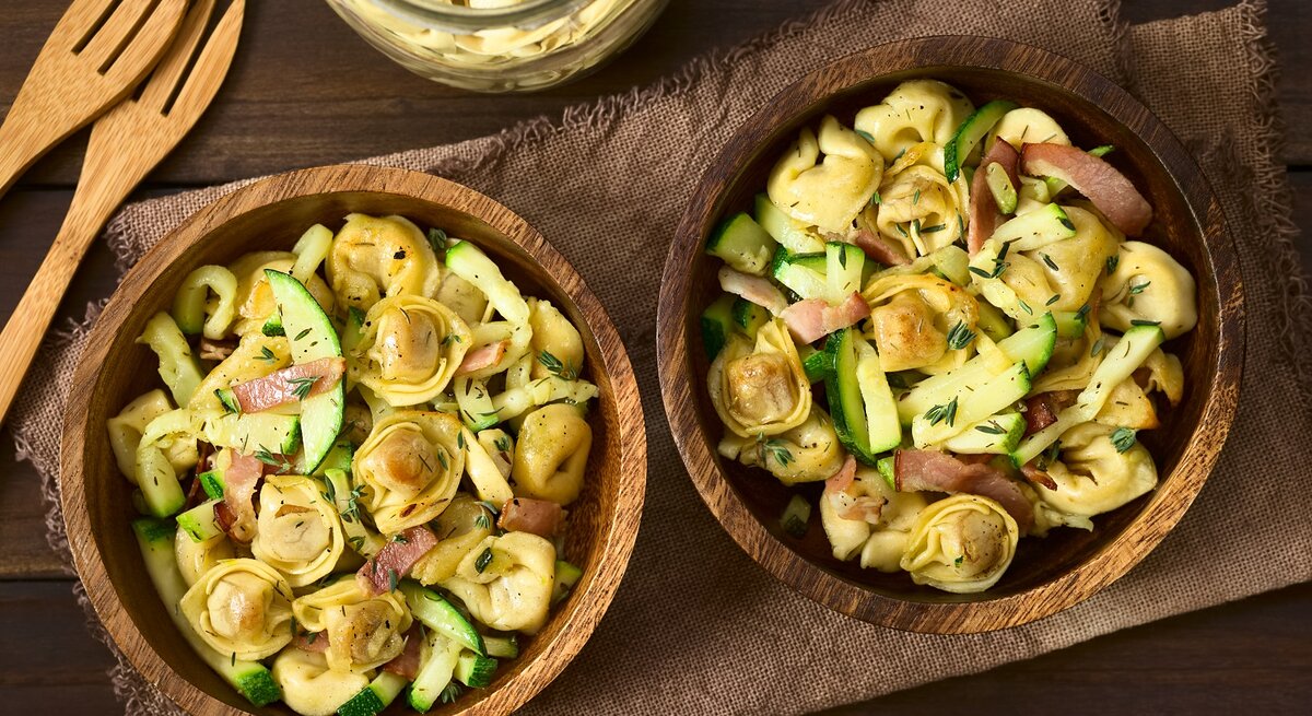 Zwei Holzschüsseln mit Tortellinisalat mit Zucchini und Speck.