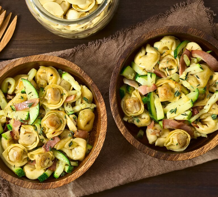 Zwei Holzschüsseln mit Tortellinisalat mit Zucchini und Speck. | © Shutterstock/Ildi Papp