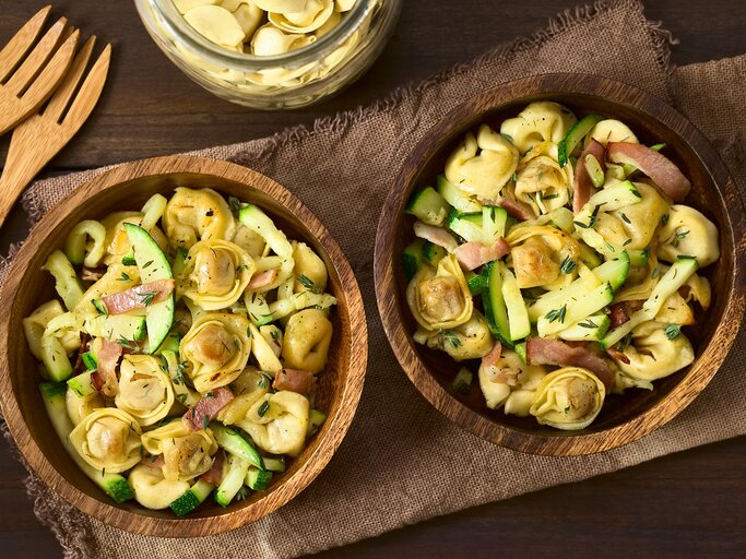 Zwei Holzschüsseln mit Tortellinisalat mit Zucchini und Speck. | © Shutterstock/Ildi Papp