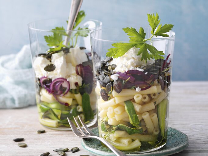 Zucchini-Makkaronisalat mit Feta im Glas. Daneben eine Gabel und im Hintergrund ein Küchentuch.  | © StockFood / für ZS Verlag / Kramp + Gölling