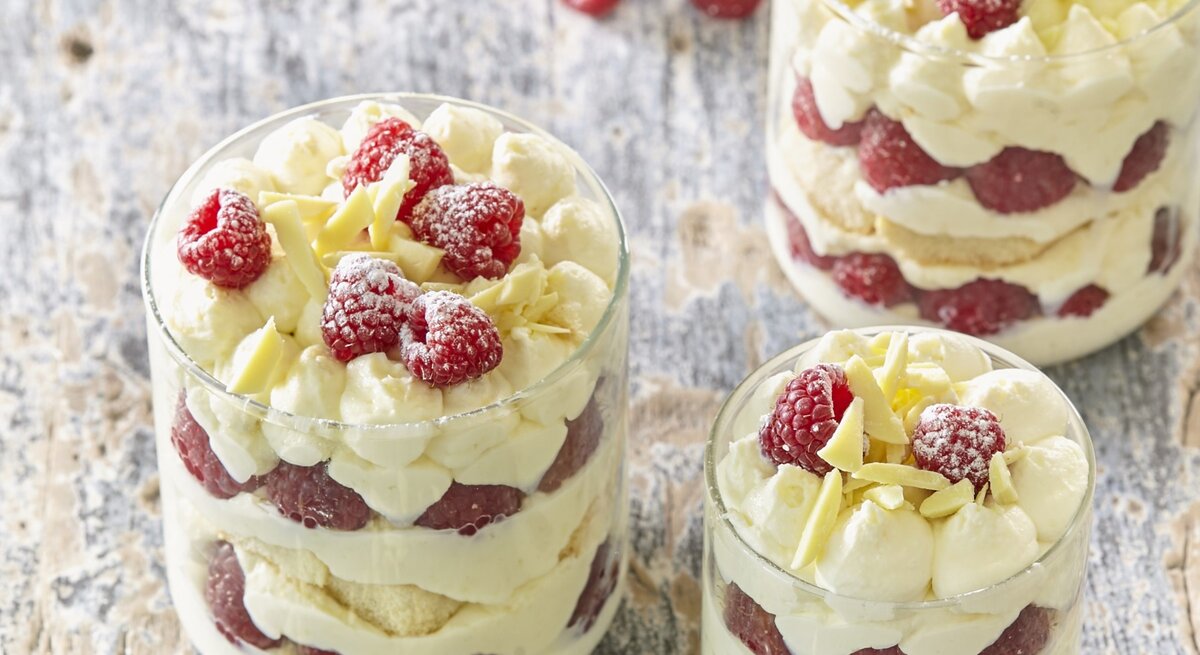 Drei kleine Gläser mit Himbeer-Tiramisu. Das Ganze auf einem hölzernen Untergrund. 