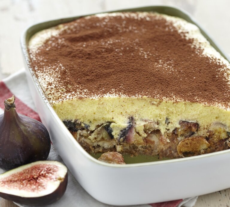 Eine Auflaufform voller Feigen-Tiramisu, angeschnitten, sodass die Feigen unter der Mascarponecreme zu sehen ist. Serviert auf einem hellen Holztisch und garniert mit Kakaopulver.  | © ockFood / PhotoCuisine / Nicoloso, Loic