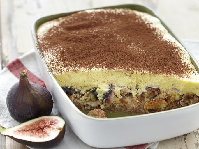 Eine Auflaufform voller Feigen-Tiramisu, angeschnitten, sodass die Feigen unter der Mascarponecreme zu sehen ist. Serviert auf einem hellen Holztisch und garniert mit Kakaopulver.  | © ockFood / PhotoCuisine / Nicoloso, Loic
