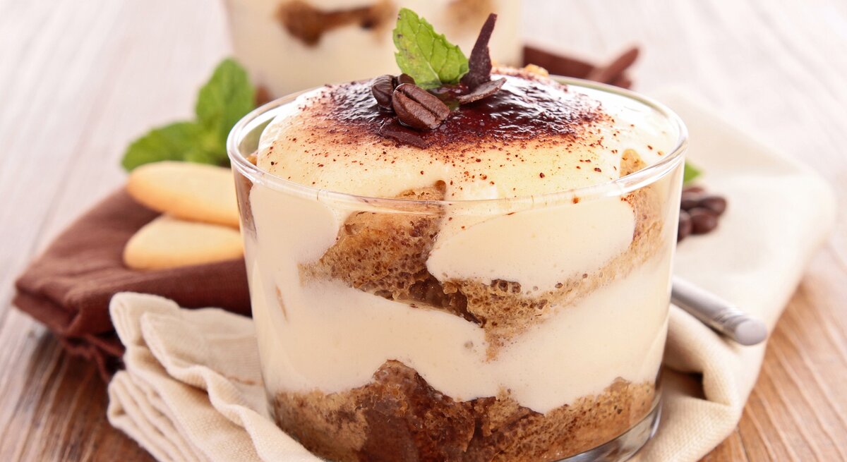 Zwei Gläser mit Biscoff-Tiramisu, bestreut mit Kakaopulver und Kaffeebohnen, geschichtet mit Karamellkeksen.
