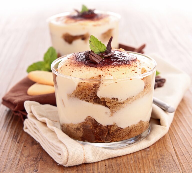 Zwei Gläser mit Biscoff-Tiramisu, bestreut mit Kakaopulver und Kaffeebohnen, geschichtet mit Karamellkeksen. | © Adobe Stock/ M.studio