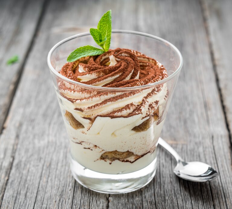 Ein durchsichtiges Glas gefüllt mit einem Dessert bestehend aus gezuckerter Kondensmilch (Milchmädchen) und Gebäck. Das Ganze steht auf einem grauen Holztisch.  | © Shutterstock/WhiteYura