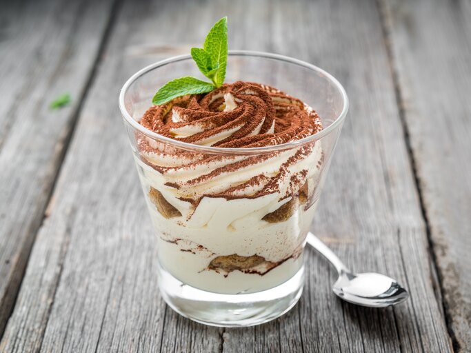 Ein durchsichtiges Glas gefüllt mit einem Dessert bestehend aus gezuckerter Kondensmilch (Milchmädchen) und Gebäck. Das Ganze steht auf einem grauen Holztisch.  | © Shutterstock/WhiteYura