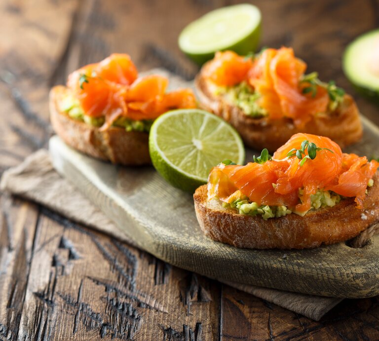 Drei Lachs-Bruschetta mit Avocado auf einem Holztablett. | © Shutterstock/MariaKovaleva