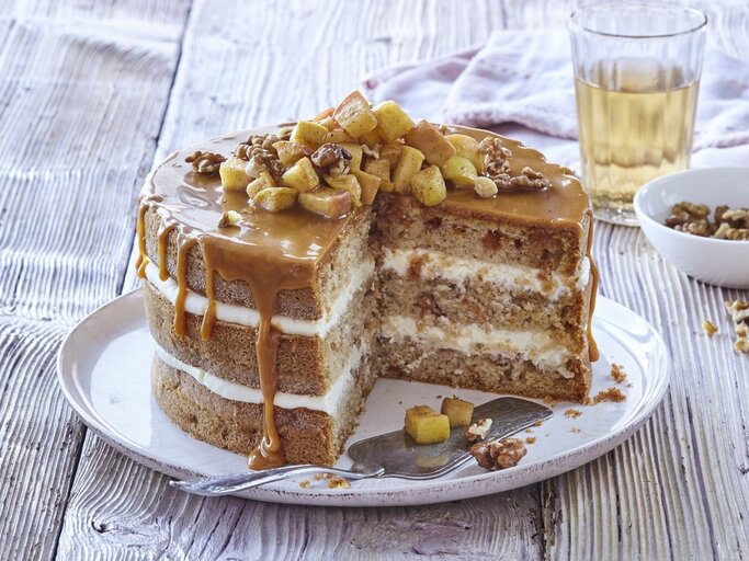 Auf einem Teller steht eine Apfel-Karamell-Schichttorte. Sie ist mit Äpfeln und Nüssen bedeckt.  | © StockFood / Profimedia