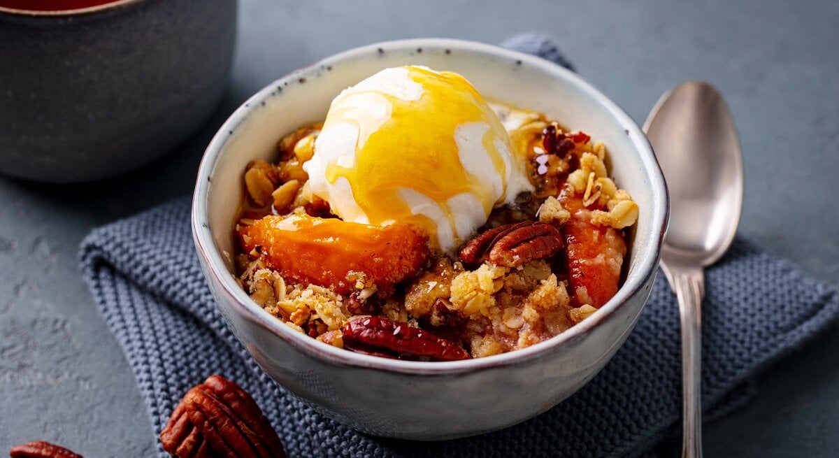Eine Schale mit Pfirsich-Crumble auf einem grauen Küchentuch.