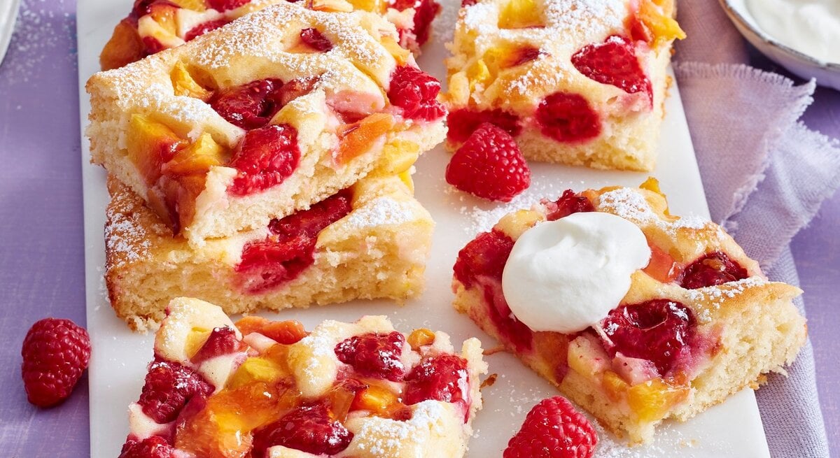 Auf einem Tisch sind mehrere Stücken Pfirsich-Melba-Kuchen serviert. Sie sind mit Puderzucker bestreut.