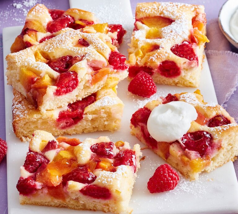 Auf einem Tisch sind mehrere Stücken Pfirsich-Melba-Kuchen serviert. Sie sind mit Puderzucker bestreut. | © EAT CLUB / Isabell Triemer