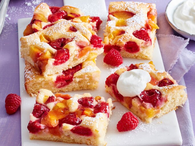 Auf einem Tisch sind mehrere Stücken Pfirsich-Melba-Kuchen serviert. Sie sind mit Puderzucker bestreut. | © EAT CLUB / Isabell Triemer