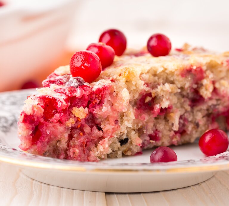Ein weißer Teller mit Verzierungen und einem Stück vom Johannisbeerkuchen auf einem hellen Holztisch seitlich fotografiert. | © Shutterstock/ Ivan Danik