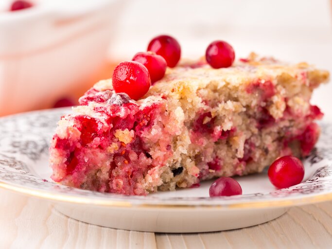Ein weißer Teller mit Verzierungen und einem Stück vom Johannisbeerkuchen auf einem hellen Holztisch seitlich fotografiert. | © Shutterstock/ Ivan Danik