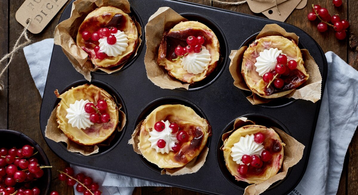 Johannisbeer-Mandel-Törtchen in einer Muffinform. Daneben liegen Johannisbeeren und ein Küchentuch. 