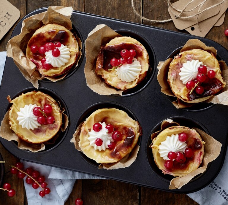 Johannisbeer-Mandel-Törtchen in einer Muffinform. Daneben liegen Johannisbeeren und ein Küchentuch.  | © EAT CLUB / Isabell Triemer