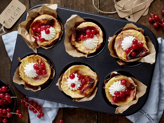 Johannisbeer-Mandel-Törtchen in einer Muffinform. Daneben liegen Johannisbeeren und ein Küchentuch.  | © EAT CLUB / Isabell Triemer