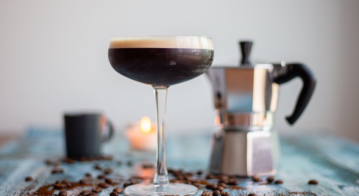 Ein Espresso Martini sowie eine Espressokanne, Kaffeebohnen und eine Kerze.