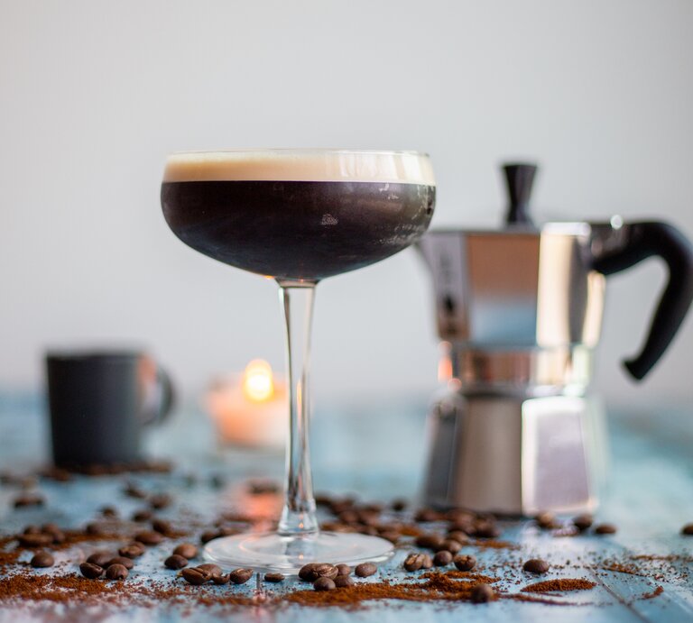 Ein Espresso Martini sowie eine Espressokanne, Kaffeebohnen und eine Kerze. | © Getty Images/ Mustafa Bugra Celik