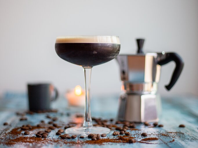 Ein Espresso Martini sowie eine Espressokanne, Kaffeebohnen und eine Kerze. | © Getty Images/ Mustafa Bugra Celik