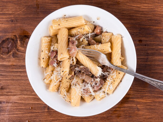 Rigatoni mit gebratenem Guanciale und Pecorino auf weißem Teller. Dieser steht auf einem Holzuntergrund.  | © Getty Images/Stanislav Ostranitsa