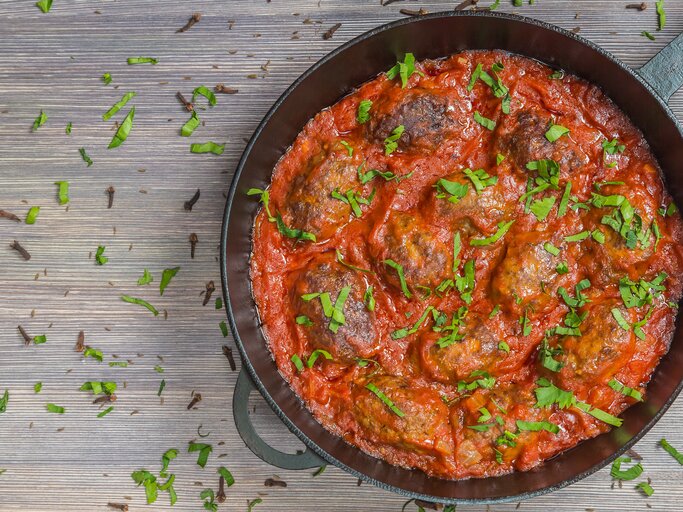 Soutzoukakia in Tomatensoße in schwarzer Pfanne auf Holztisch.  | © Shutterstock/starets