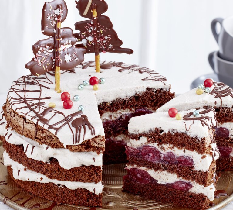 Schwarzwälder Glühwein-Kirschtorte, angeschnitten serviert auf einem Servierteller, dekoriert mit Weihnachtlichem Schmuck wie Lebkuchen und kandierten Kirschen.  | © EAT CLUB / Isabell Triemer