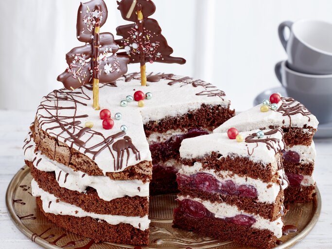 Schwarzwälder Glühwein-Kirschtorte, angeschnitten serviert auf einem Servierteller, dekoriert mit Weihnachtlichem Schmuck wie Lebkuchen und kandierten Kirschen.  | © EAT CLUB / Isabell Triemer