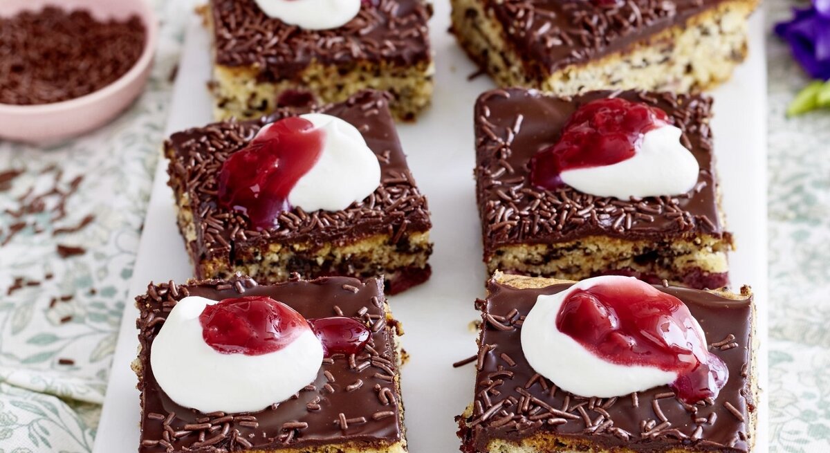 Auf einer Platte liegen mehrere Stücke des Kirsch-Ameisenkuchen. Er ist mit Sahne und roter Grütze verziert.
