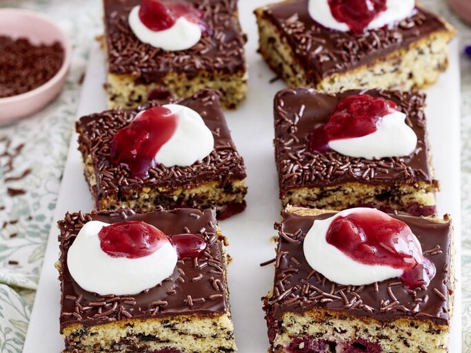 Auf einer Platte liegen mehrere Stücke des Kirsch-Ameisenkuchen. Er ist mit Sahne und roter Grütze verziert. | © EAT CLUB / Isabell Triemer