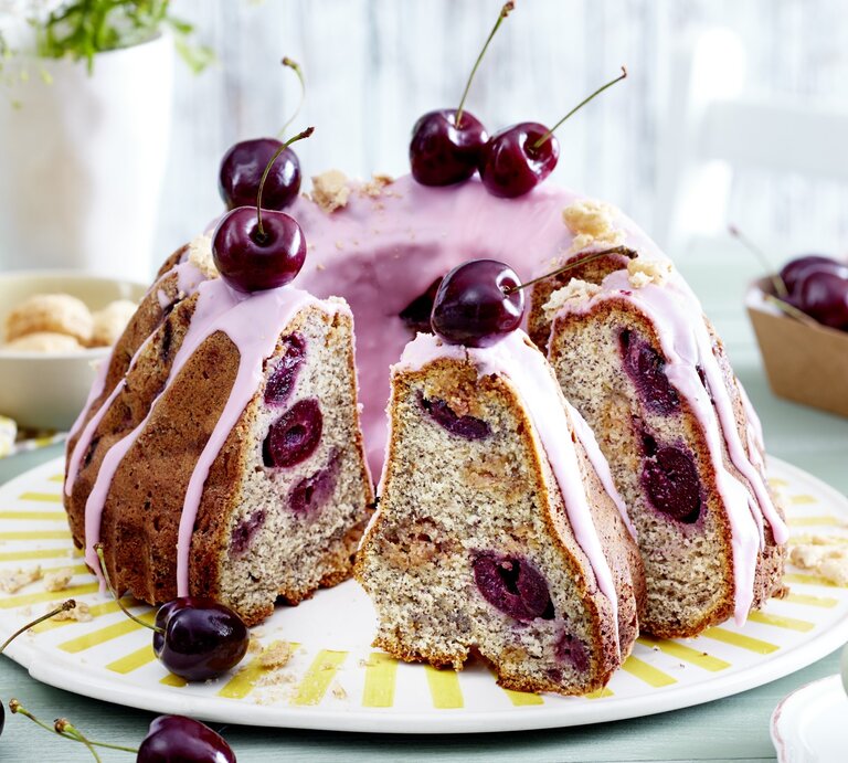 Ein Schmand-Mohnkuchen mit Kirschen auf einem weißen flachen Teller. | © EAT CLUB/Isabell Triemer