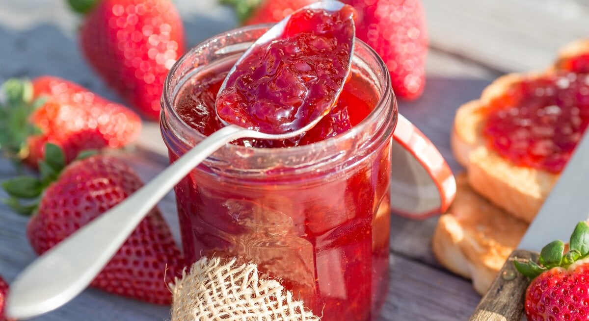 Ein Glas Erdbeer-Aperol-Marmelade ist mit Löffel, Erdbeeren und Toast.