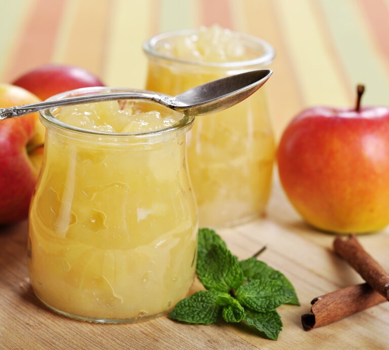 Zwei Gläser Apfel-Minz-Marmelade stehen auf einem Holzbrett. Drumherum liegen Äpfel. | © Shutterstock / mama_mia